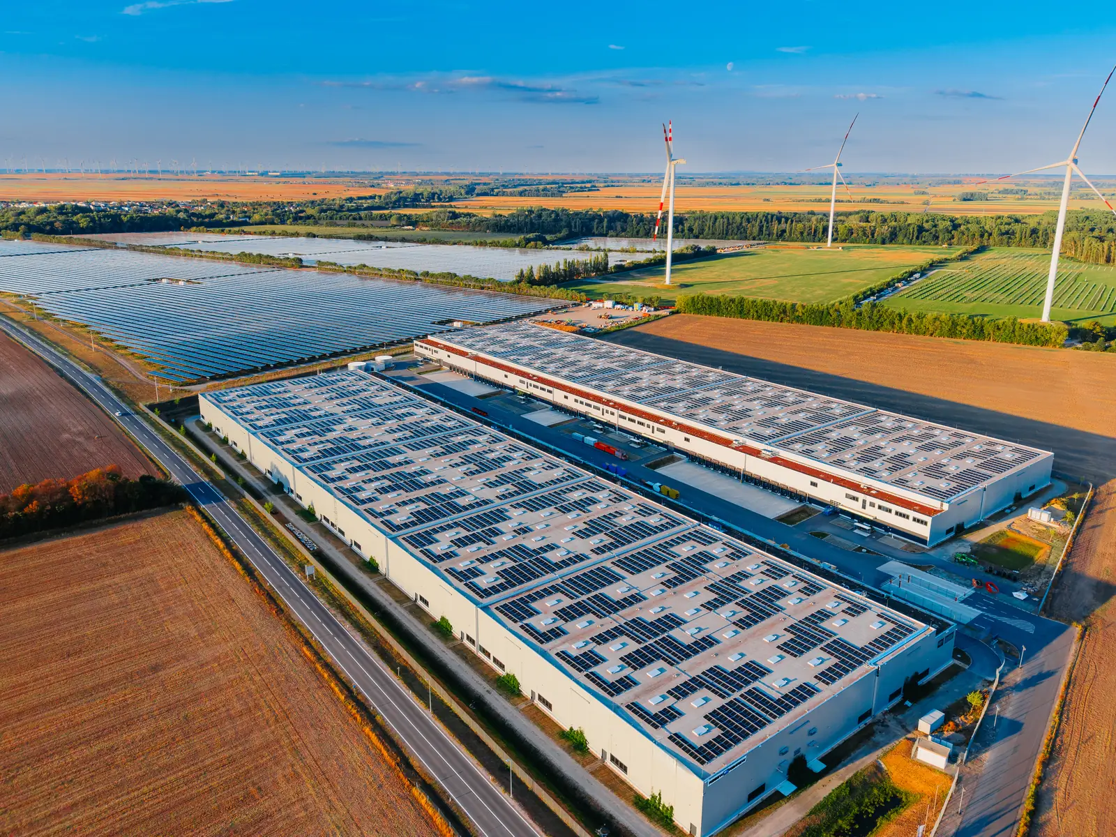 Luchtfoto van een bedrijventerrein met zonnepanelen op de bedrijfsdaken, een zonneveld ernaast en windturbines in het achterland
